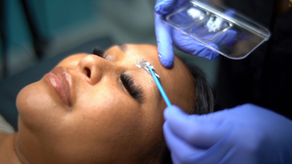 Close-up image of a med spa beautician using a microblading tool to create hair-like strokes on a client's eyebrow. This semi-permanent procedure will fill in sparse brows and create a natural-looking shape.